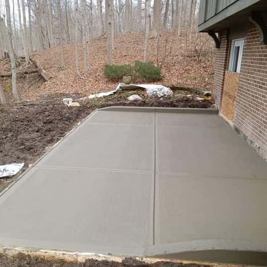 New broom-finished patio slab behind a brick home at the edge of the woods — JFC Concrete LLC, Indianapolis, IN