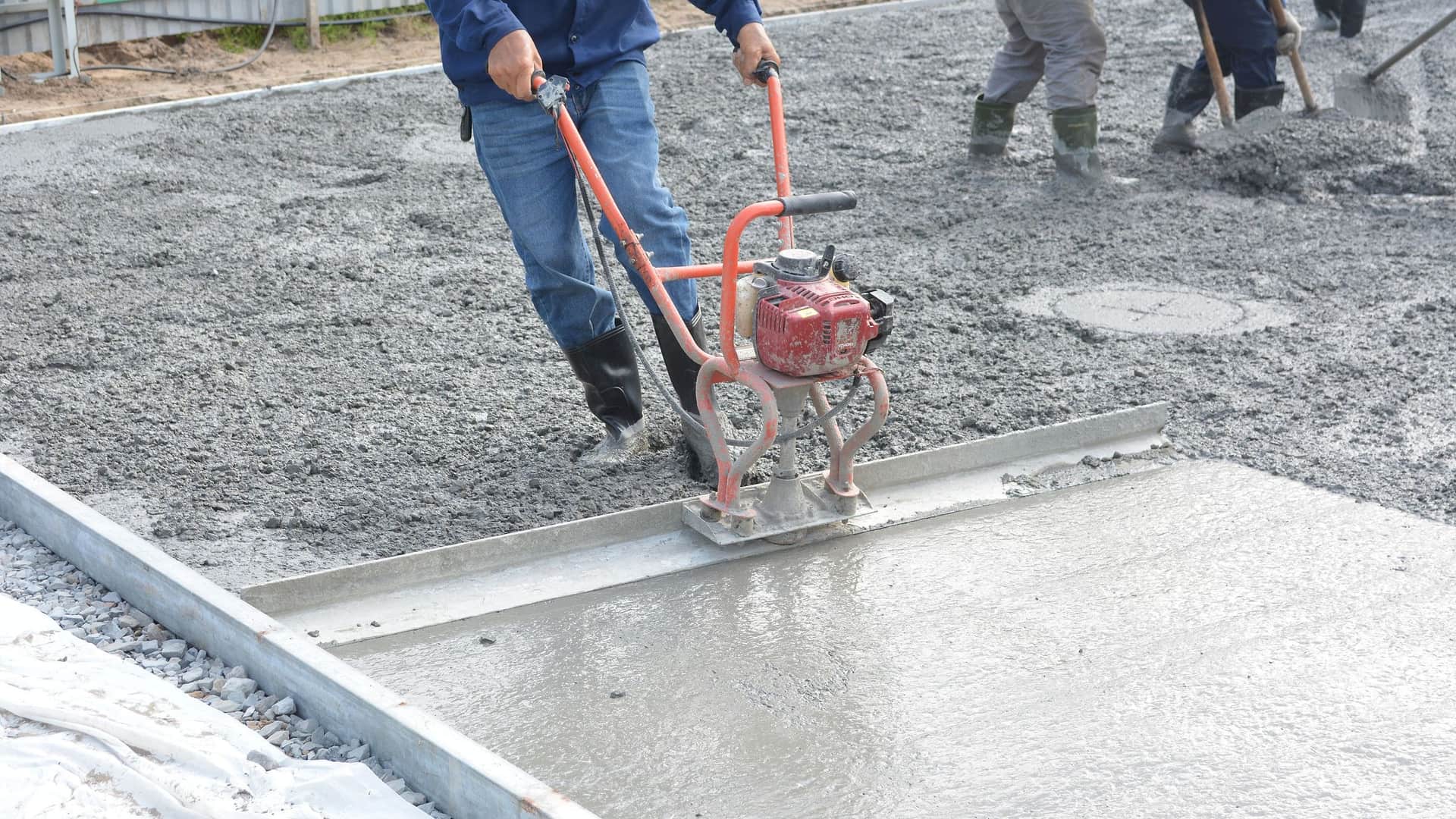 A concrete crew leveling a freshly poured slab with a power screed